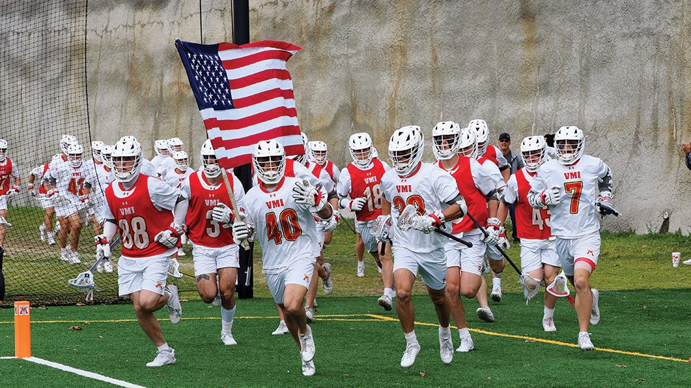 lacrosse team running across the field with American flag