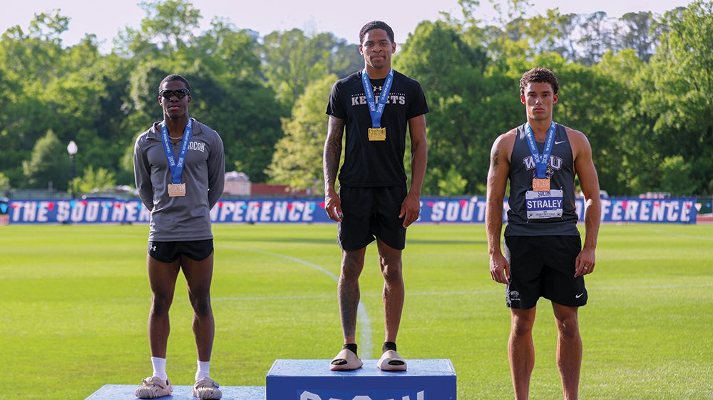 three male track and field athletes standing on winners' podium