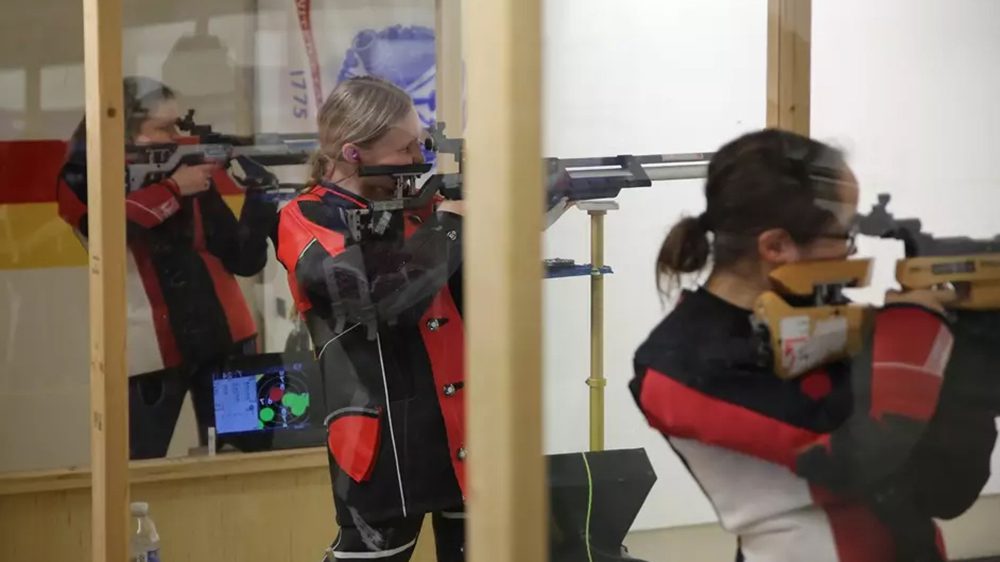 three rifle athletes standing in a row, aiming rifles at targets