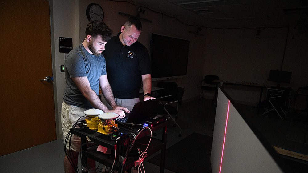 cadet and professor looking at computer screen, laser projected on screen in front of them