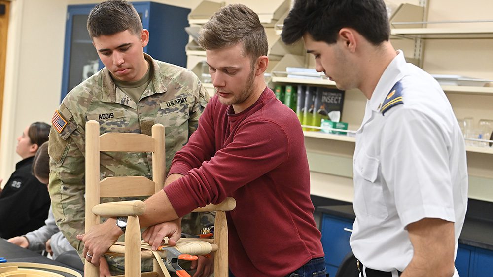 Man instructs two cadets on splint bottom weave caning during their botany class.